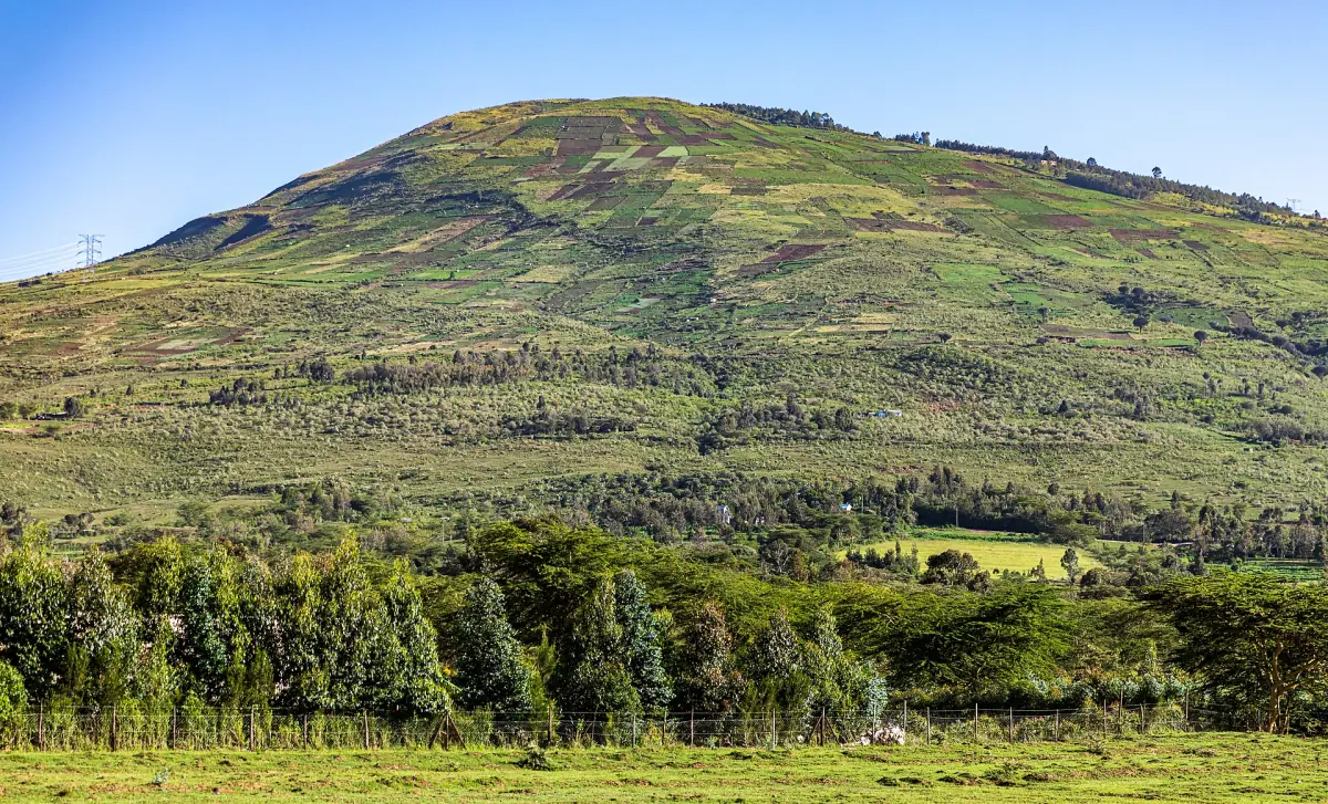 Green rounded hill rising above acacia woodland in the Rift Valley